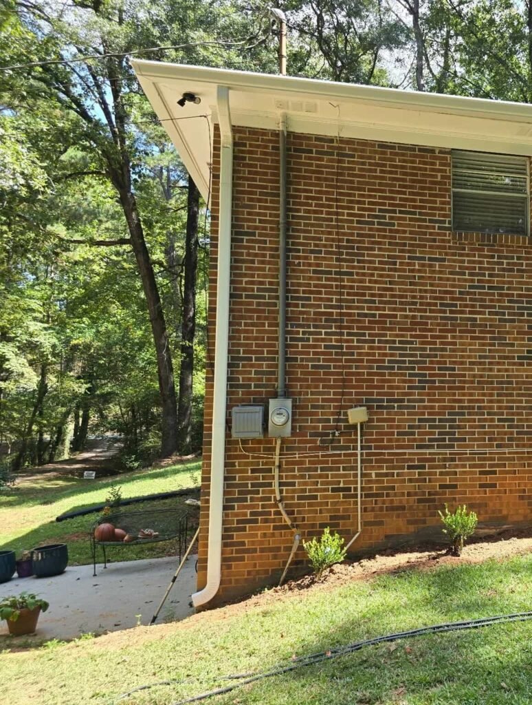 Brick home with a seamless aluminum gutter and downspout installed to direct rainwater away from the foundation on a wooded Middle Georgia property.