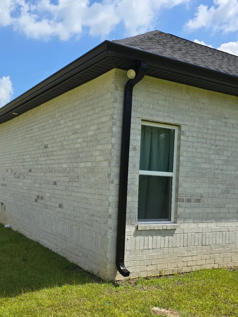 White brick home with black seamless aluminum gutter and downspout installed to improve drainage and protect the exterior in Middle Georgia.