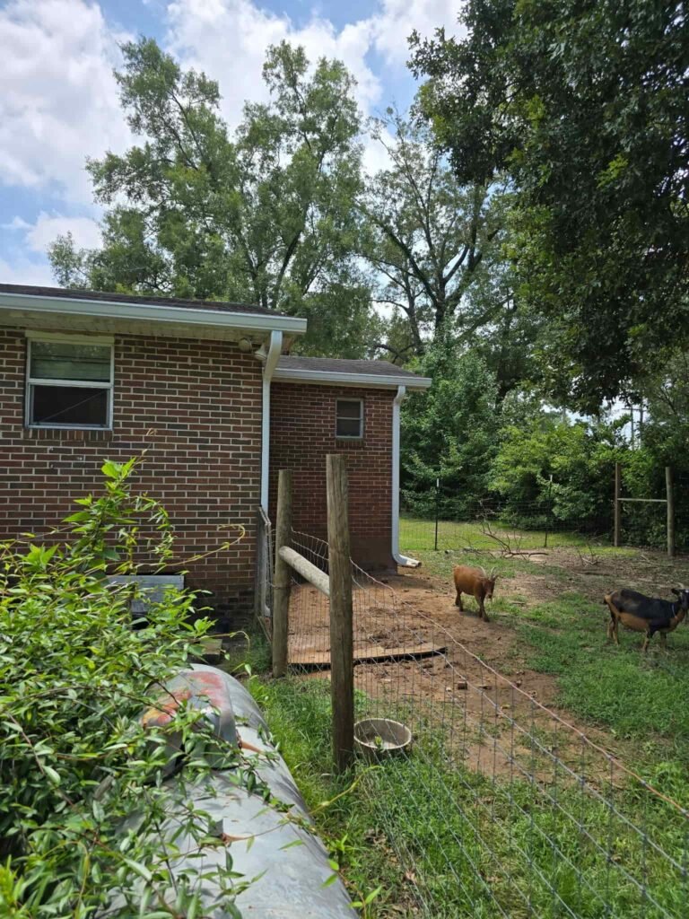 Backyard view of a brick home with a seamless aluminum gutter and downspout installed to improve drainage and protect the foundation in Middle Georgia.
