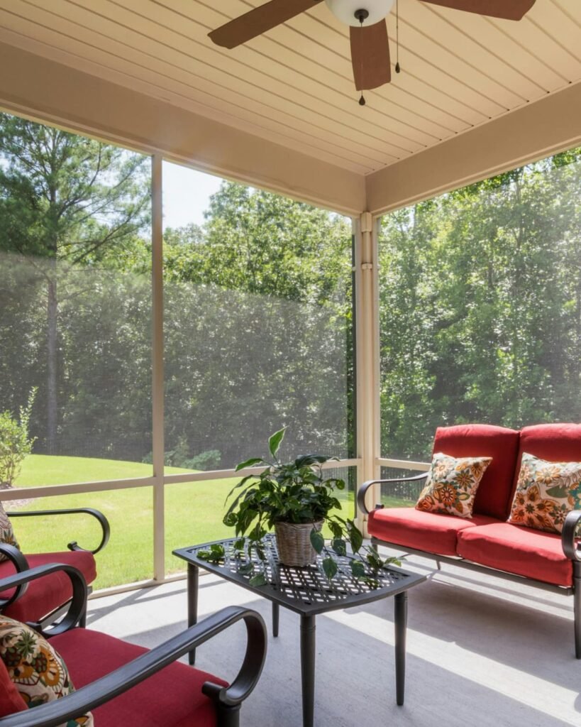 Screened-in porch overlooking a wooded backyard, showing a clean soffit and ceiling area where seamless gutters help protect outdoor living spaces from water damage.