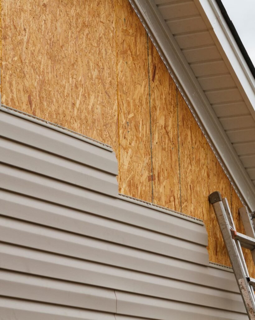 Home exterior with siding removed to expose damaged sheathing near the roofline, showing an area where proper gutter installation helps prevent water intrusion and wood rot.