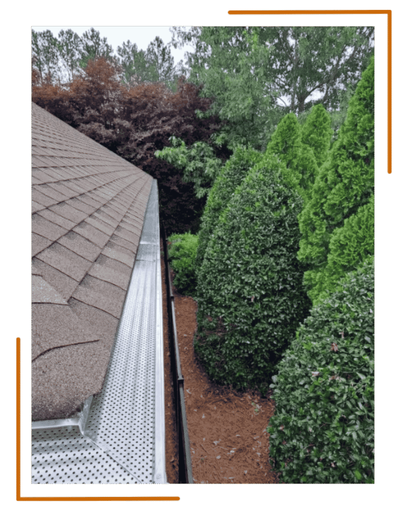 Shur Flo gutter covers installed along a roofline beside dense landscaping, providing debris protection and improved water flow for a home in Middle Georgia.