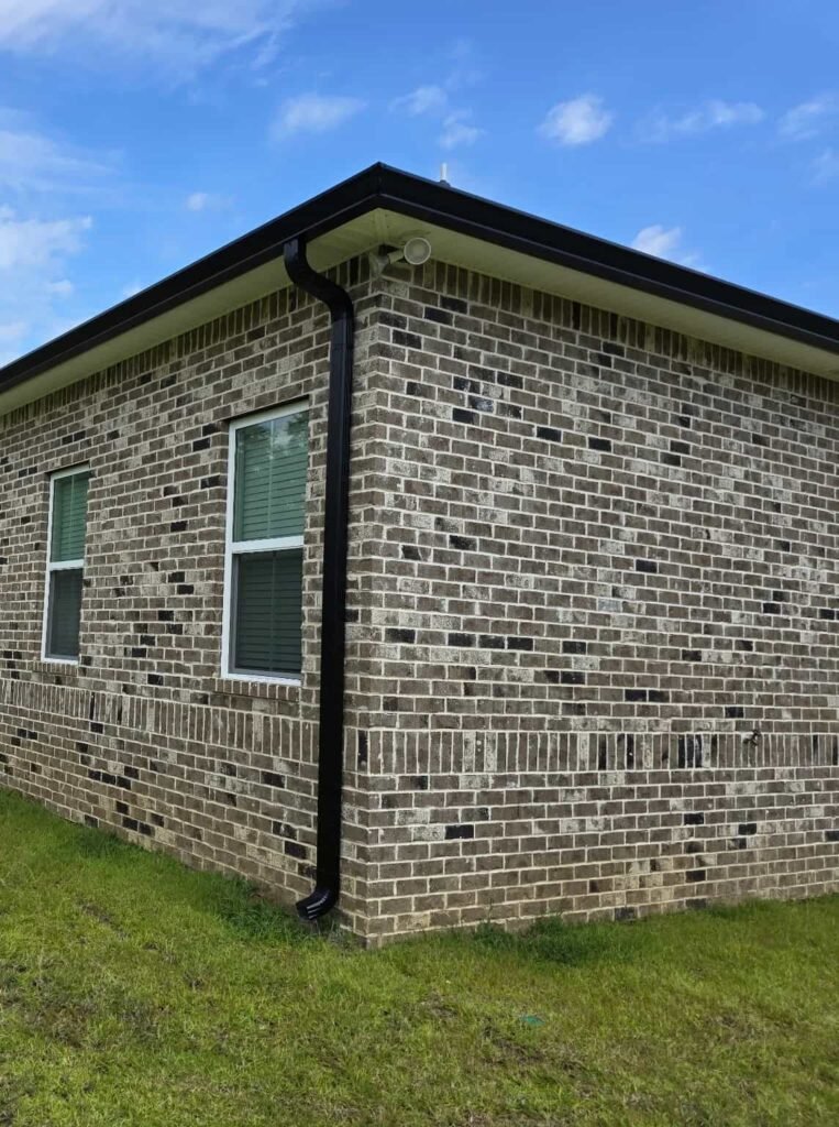 Brick home with black seamless aluminum gutter and downspout installed to improve drainage and protect the foundation in Middle Georgia.