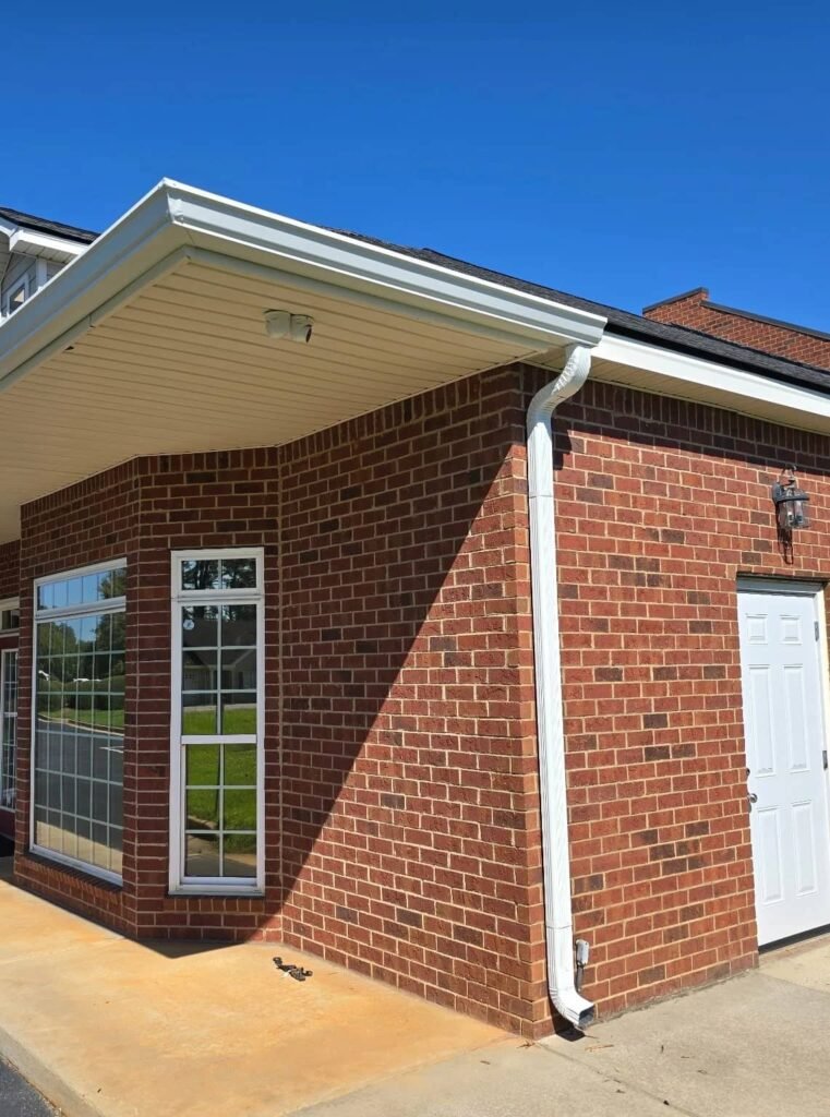 Brick commercial building with a white seamless aluminum gutter and downspout installed to improve drainage and protect the exterior in Middle Georgia.
